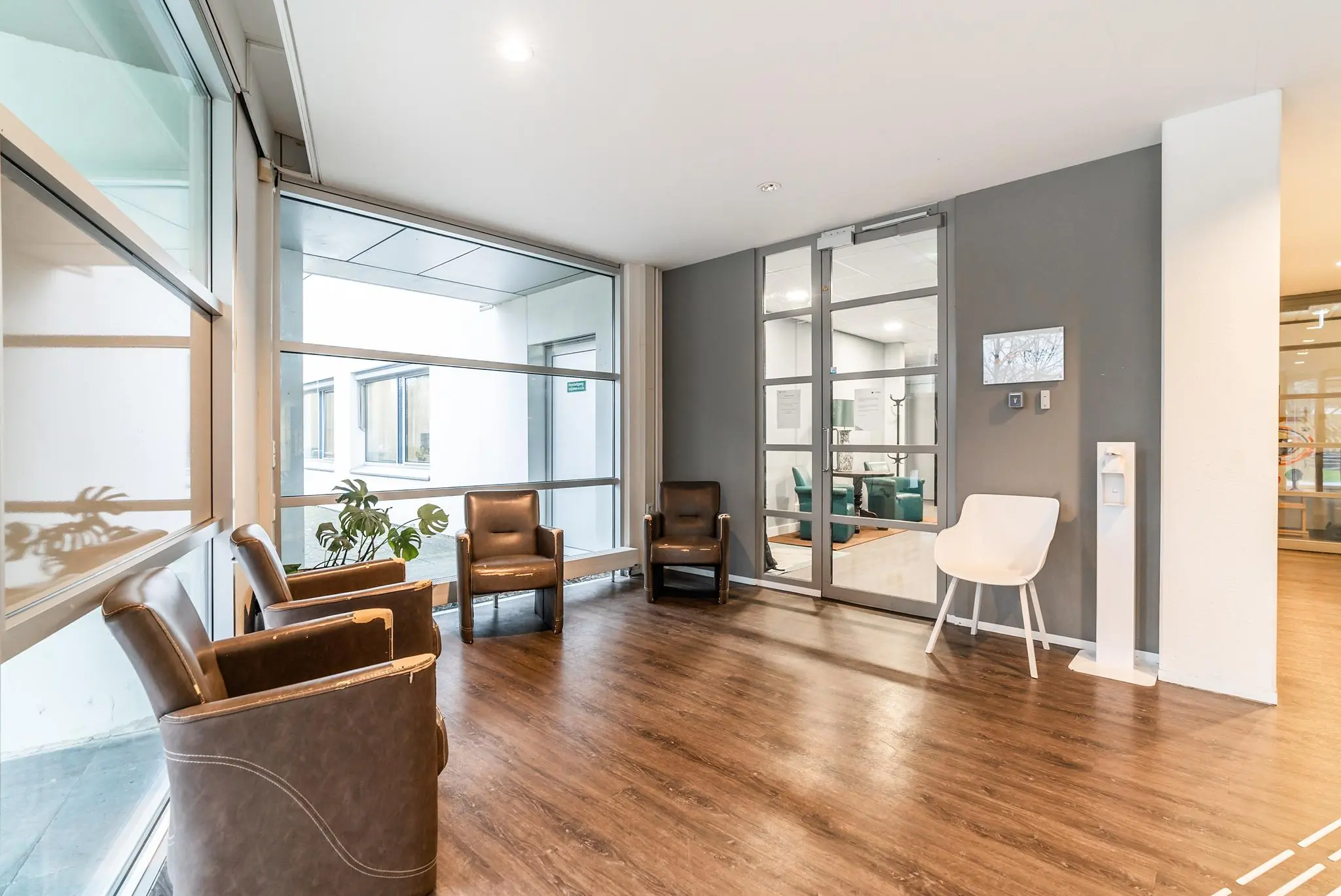 Wachtruimte met stoelen, grote ramen en toegang tot een andere ruimte in een modern kantoorpand aan de Bordewijklaan.