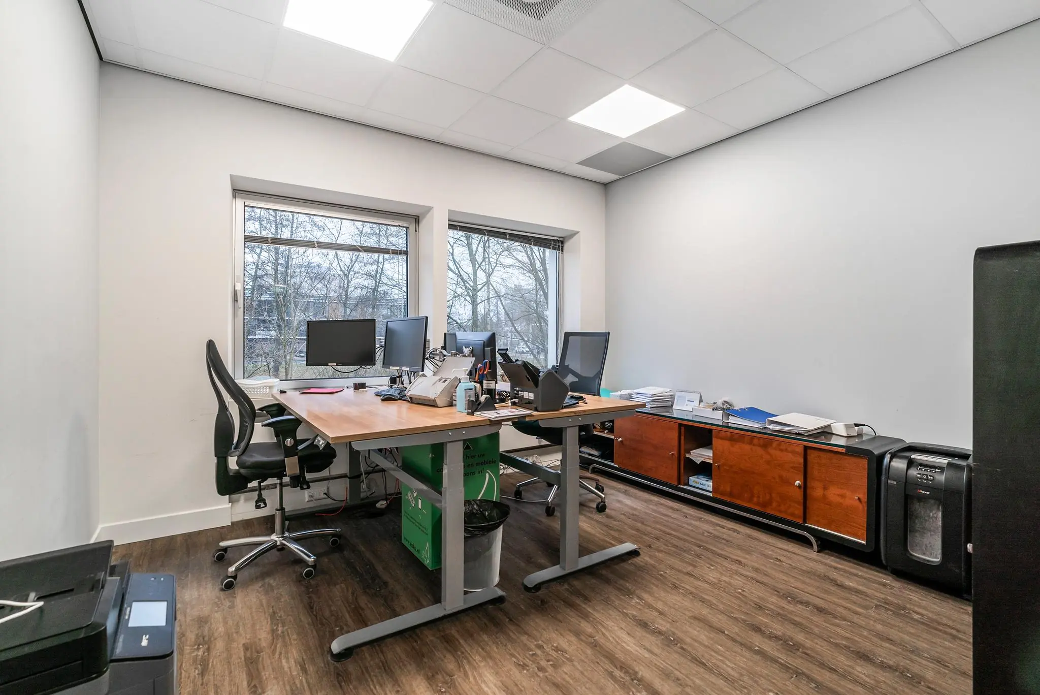 Modern kantoor met twee bureaus, meerdere computerschermen en een groot raam met uitzicht op bomen aan de Bordewijklaan.