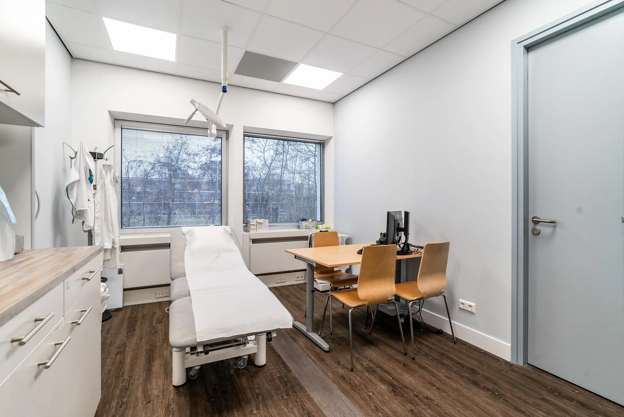 Een moderne medische spreek- en behandelkamer aan de Bordewijklaan met onderzoeksbank, bureau en computer.