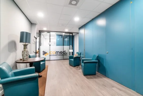 Wachtkamer van huisartsenpraktijk Comed met blauwe stoelen, een tafellamp en glazen deur met logo.