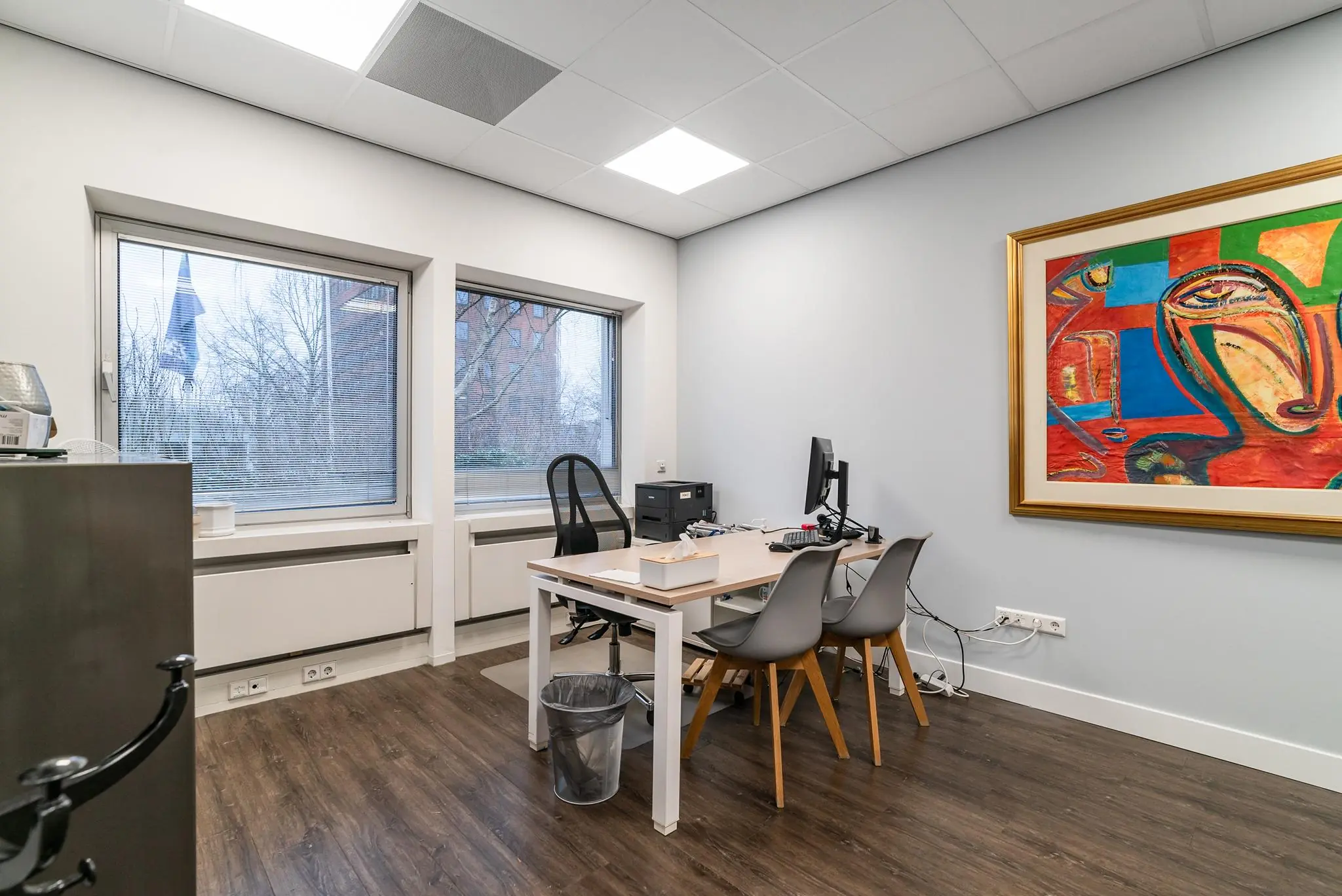 Moderne kantoorruimte aan de Bordewijklaan met bureau, stoelen, computer en kleurrijk schilderij aan de muur.