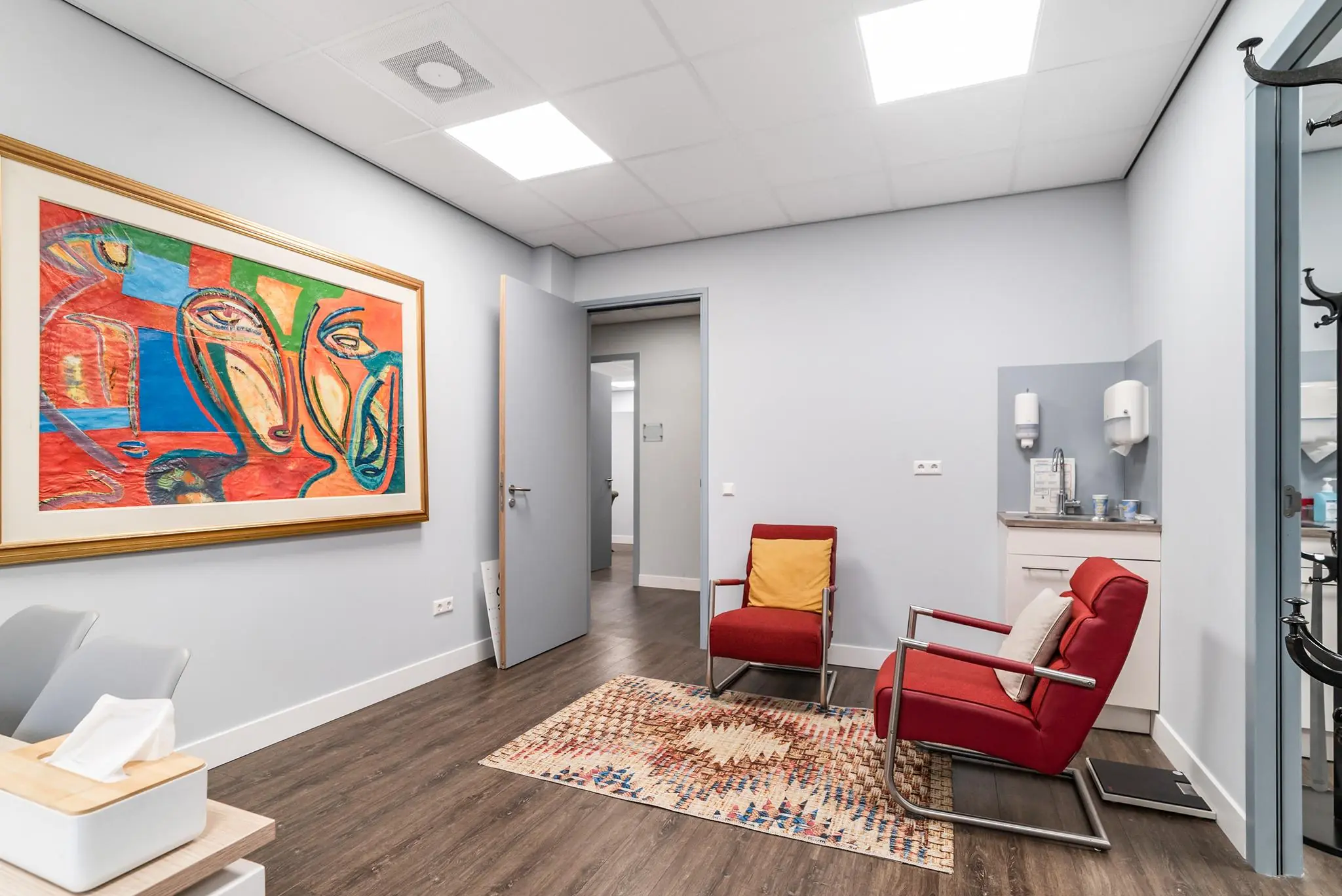 Smaakvol ingerichte wachtruimte aan de Bordewijklaan met moderne stoelen, kleurrijk schilderij en een koffiehoekje.