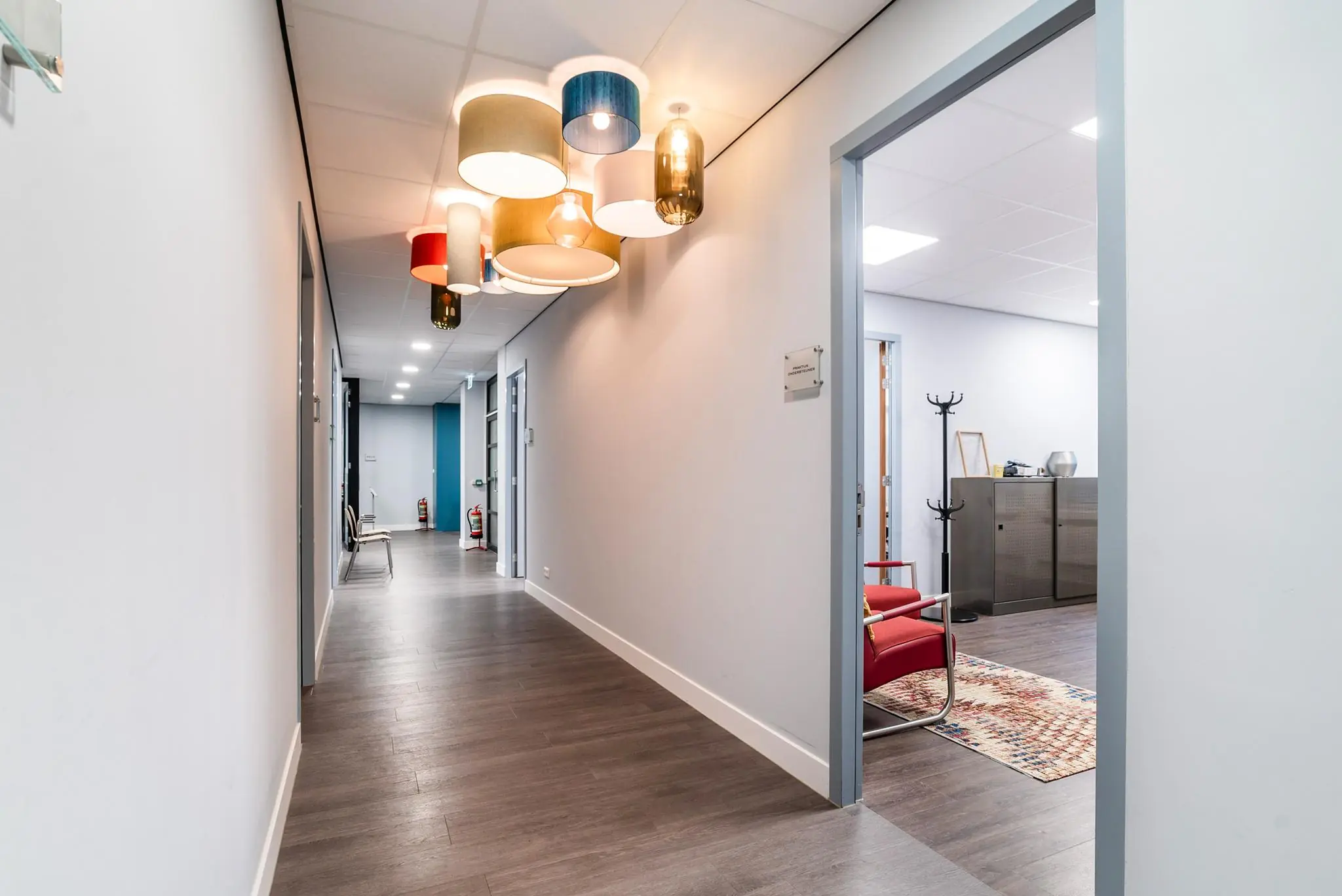 Modern kantoorinterieur aan de Bordewijklaan met houten vloer, kleurrijke plafondlampen en zicht op meerdere kantoorruimtes.