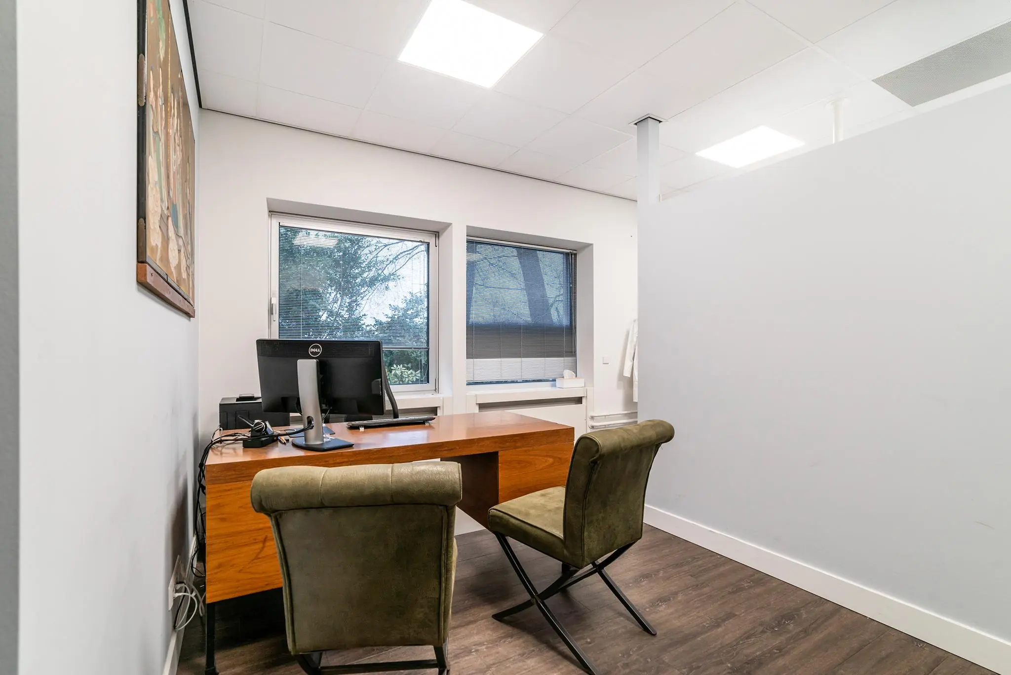 Moderne spreekkamer aan de Bordewijklaan met houten bureau, twee stoelen en uitzicht op buiten via grote ramen.
