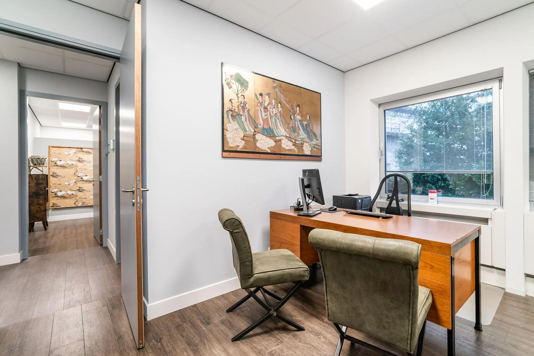 Modern kantoor aan de Bordewijklaan met houten bureau, twee stoelen en Aziatisch wandkunstwerk.
