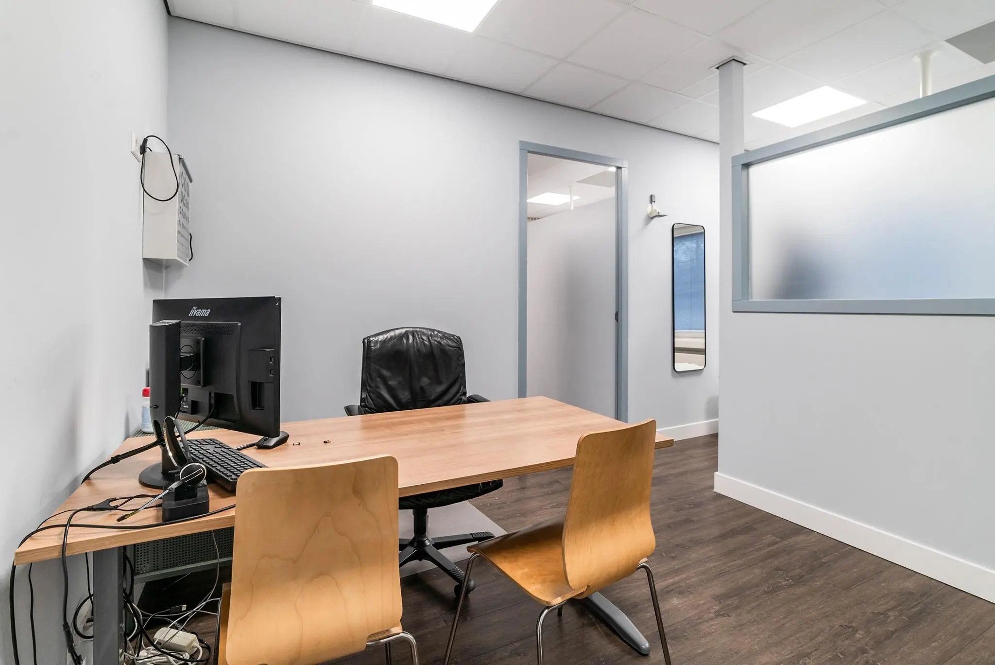 Moderne kantoorruimte aan de Bordewijklaan met een houten bureau, twee stoelen, computer en glazen scheidingswand.