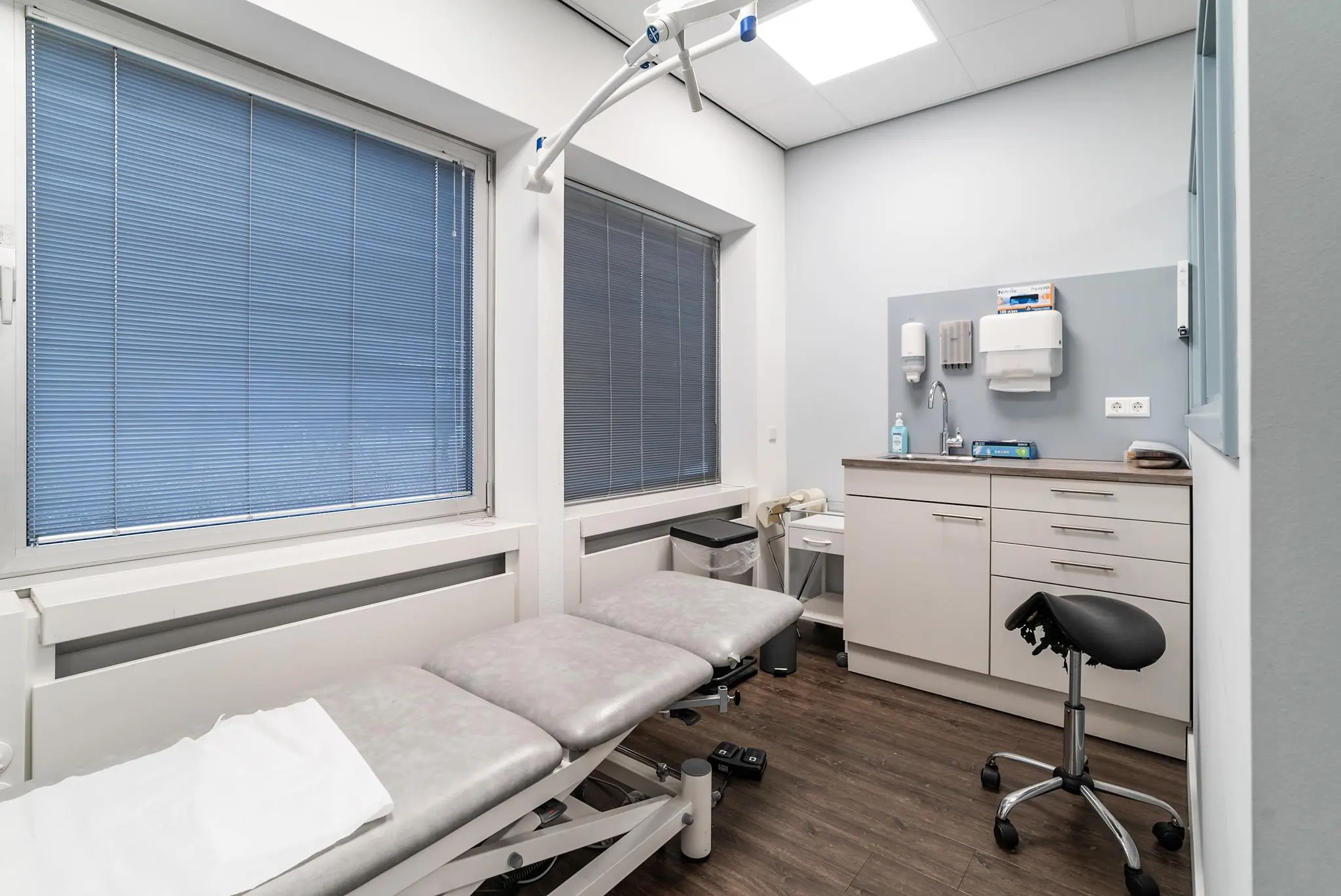 Moderne, steriele behandelkamer in een medische praktijk aan de Bordewijklaan met onderzoeksbank, wastafel en medische benodigdheden.