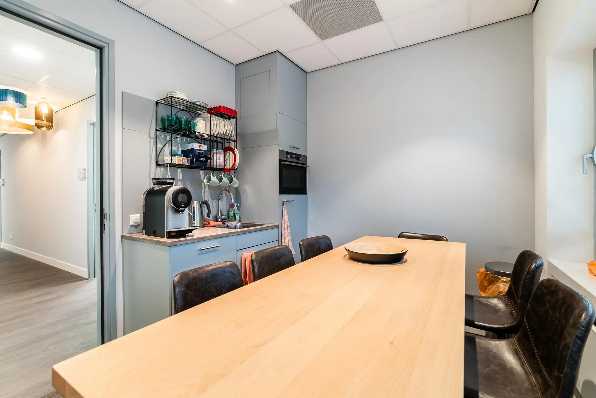 Moderne pantry met koffiezetapparaat, eettafel en ingebouwde keukenapparatuur aan de Bordewijklaan.
