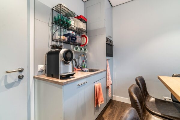 Moderne kitchenette aan de Bordewijklaan met koffiezetapparaat, spoelbak, oven en open wandrek met servies.