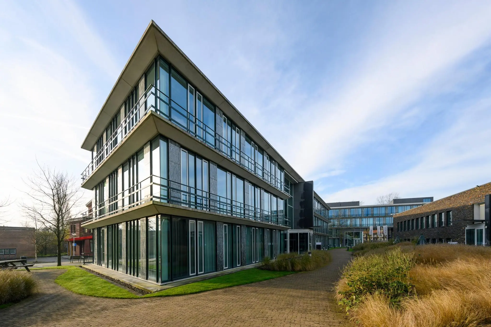 Modern kantoorgebouw aan de De Cuserstraat met glazen gevels en groene wandelpaden.