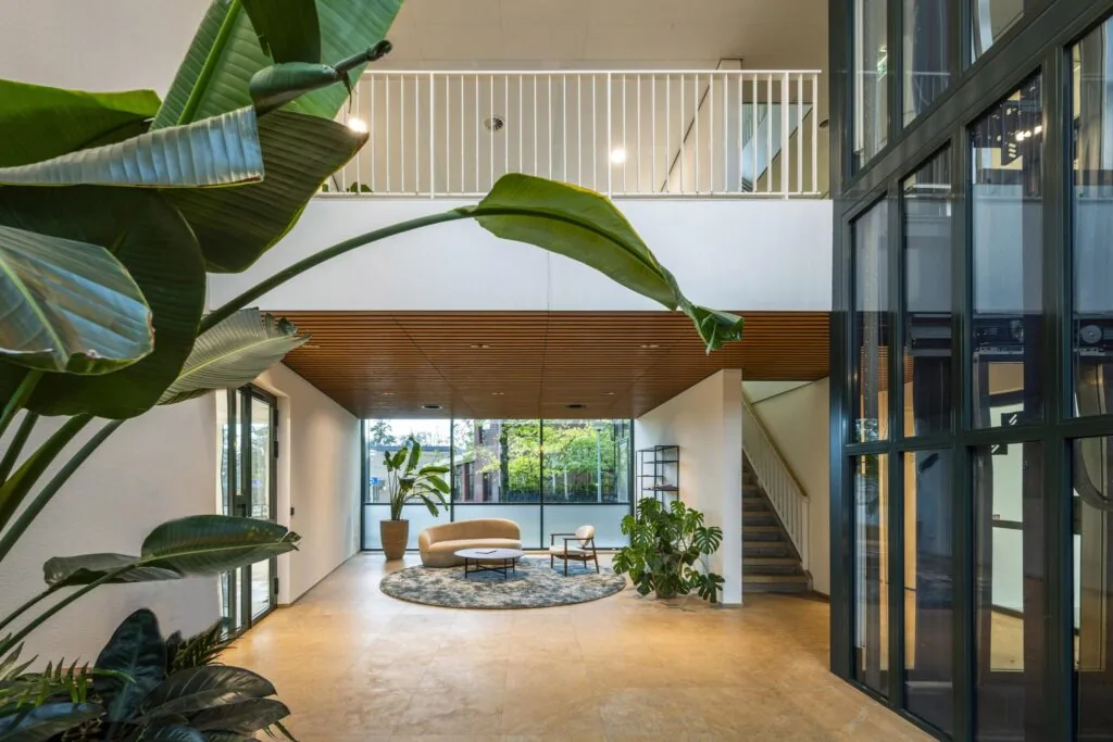 Moderne en lichte ontvangsthal aan de De Cuserstraat met zithoek, grote planten en een glazen lift.