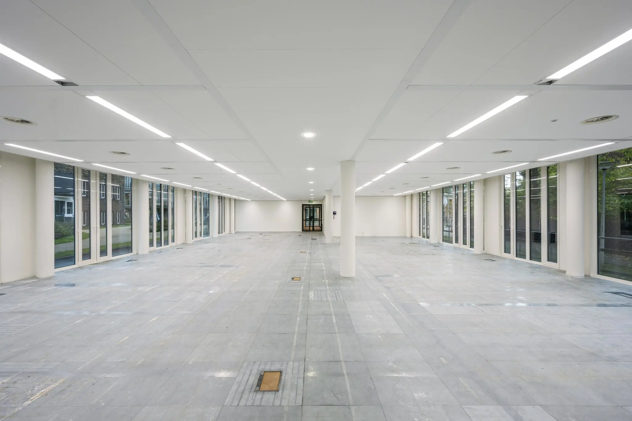 Leeg, modern kantoorpand aan de De Cuserstraat met grote ramen en systeemplafondverlichting.