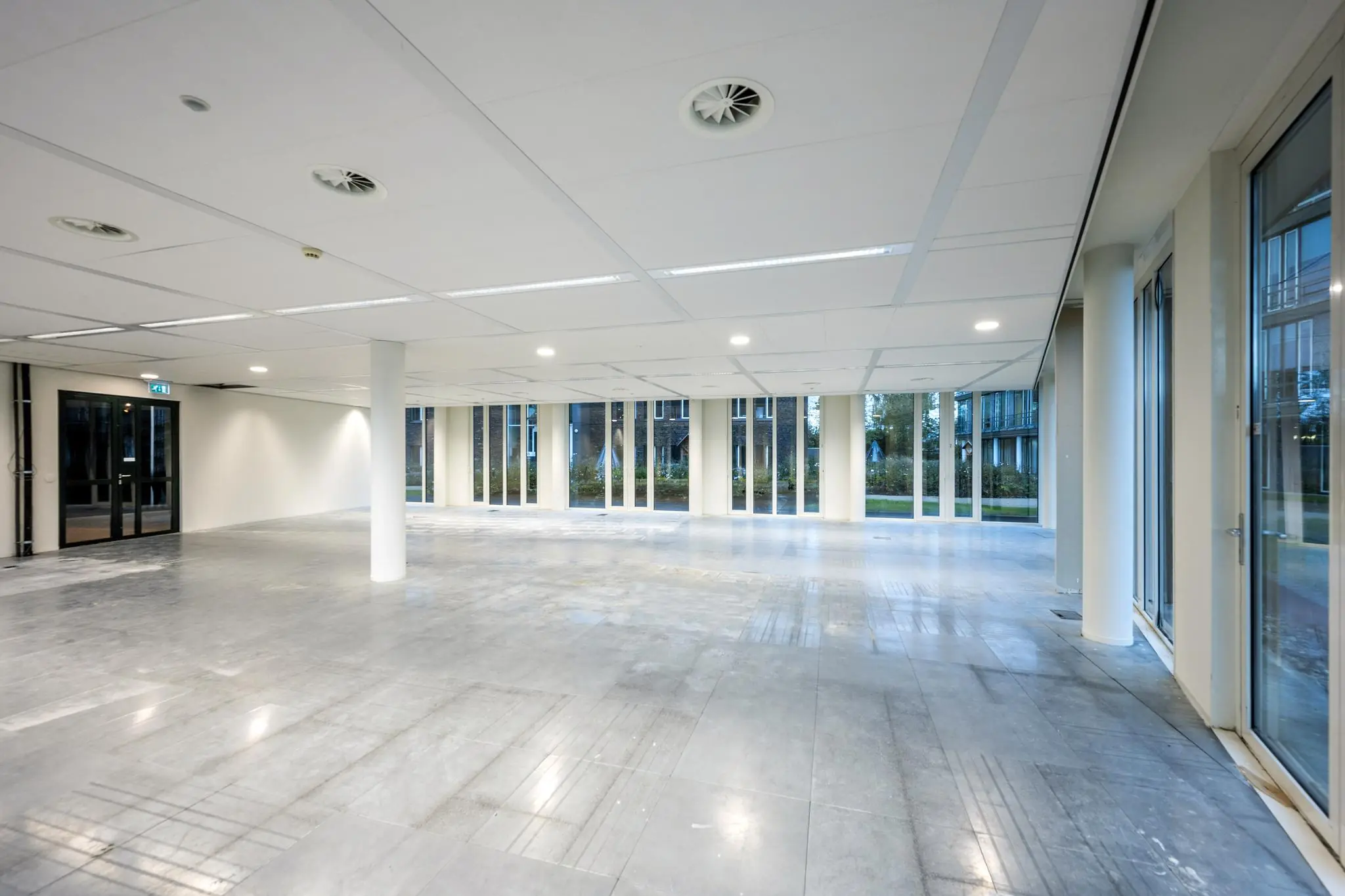 Leegstaand, modern kantoorruimte-interieur aan de De Cuserstraat met grote ramen en een grijze tegelvloer.