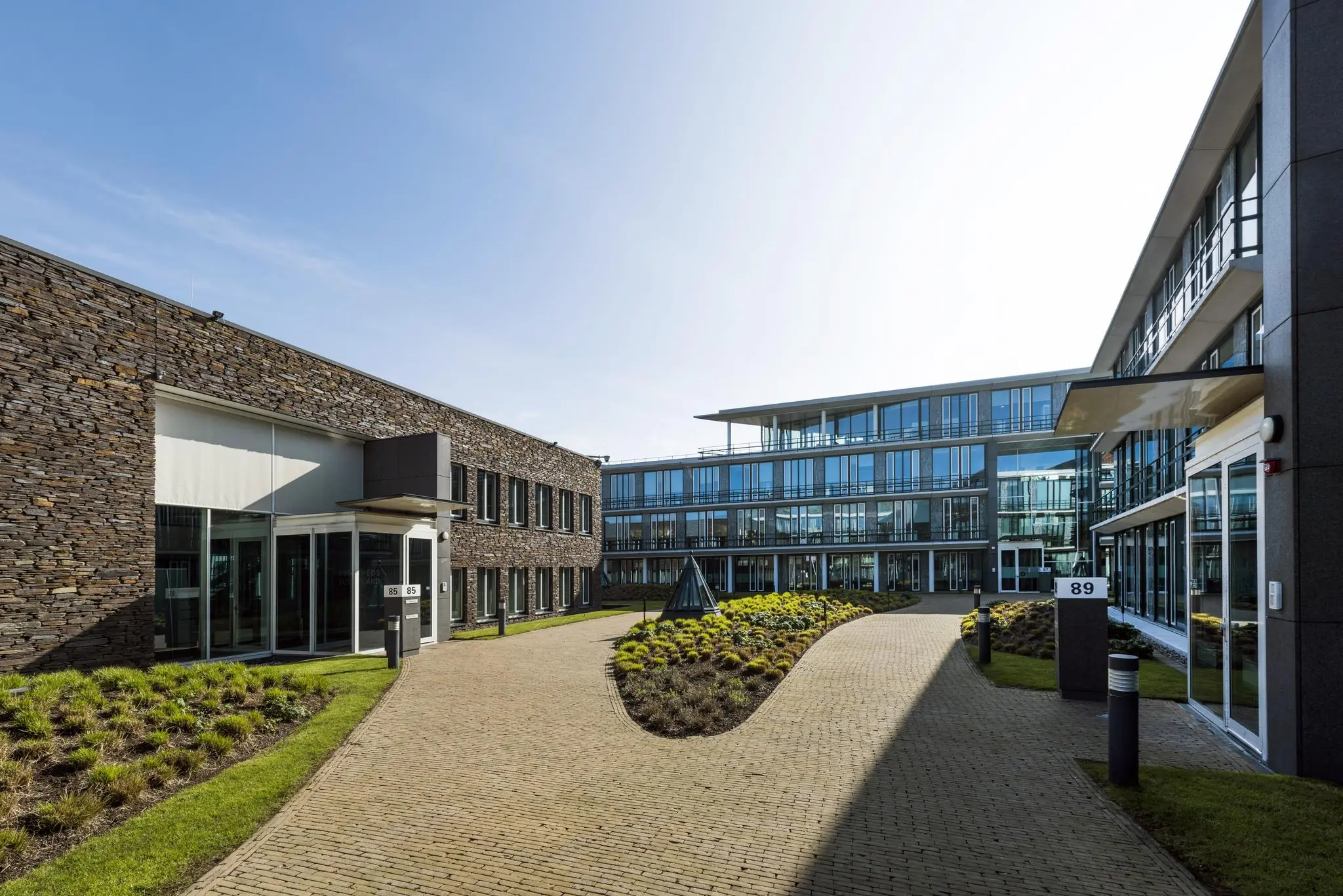 Moderne kantoorgebouwen aan de De Cuserstraat met een verzorgde, groene binnentuin en glazen gevels.
