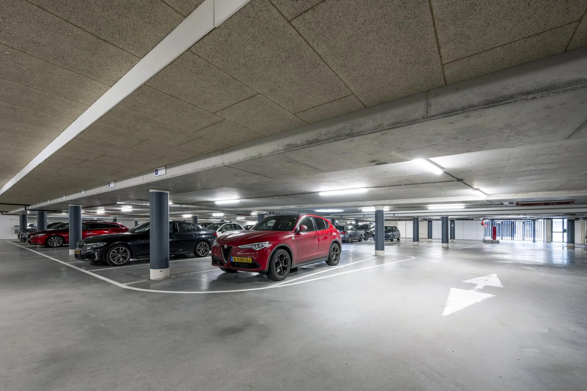 Ondergrondse parkeergarage aan de De Cuserstraat met geparkeerde auto's, waaronder een rode SUV op de voorgrond.