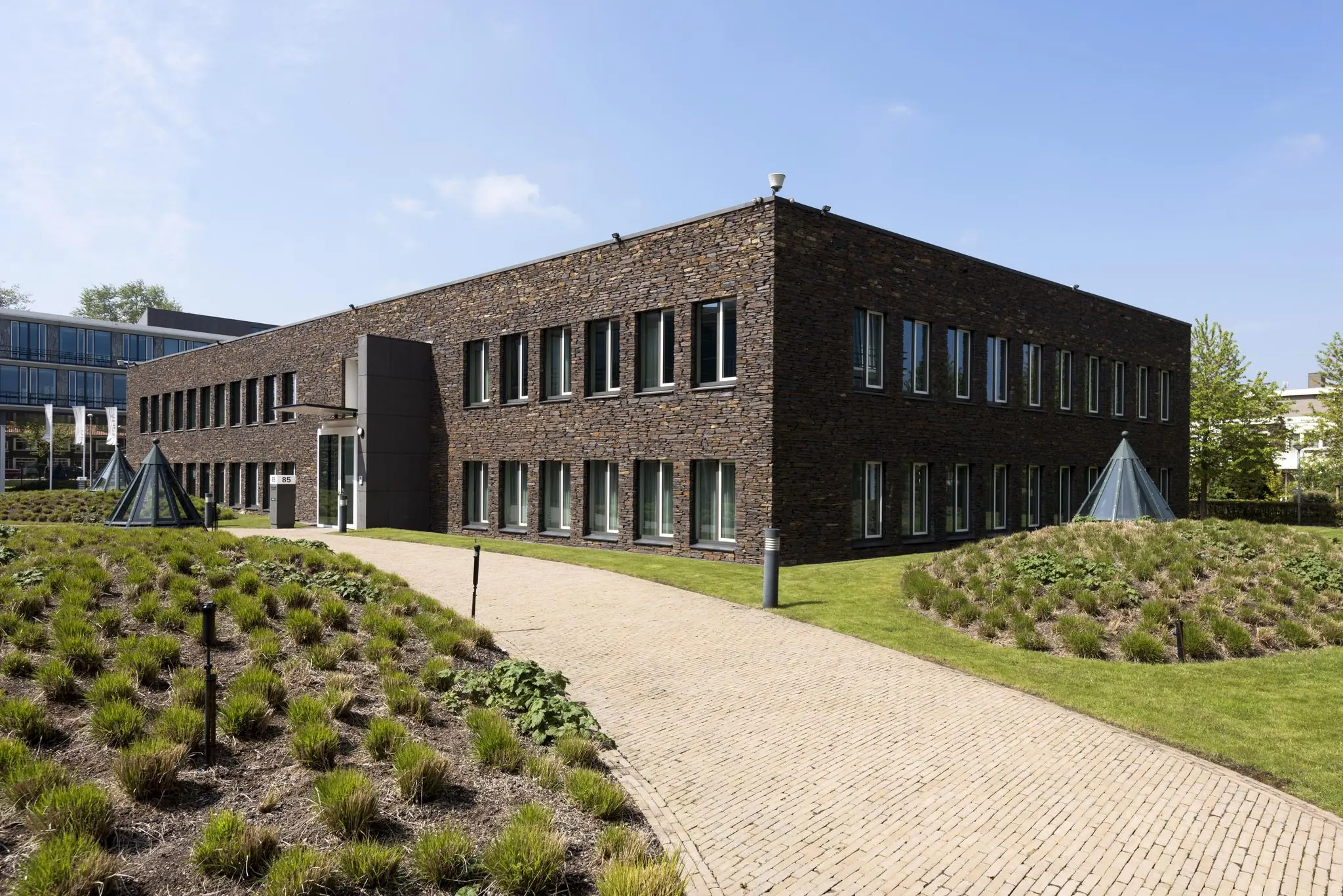 Modern kantoorgebouw aan de De Cuserstraat met bakstenen gevel, omgeven door een verzorgde tuin en glazen koepels.