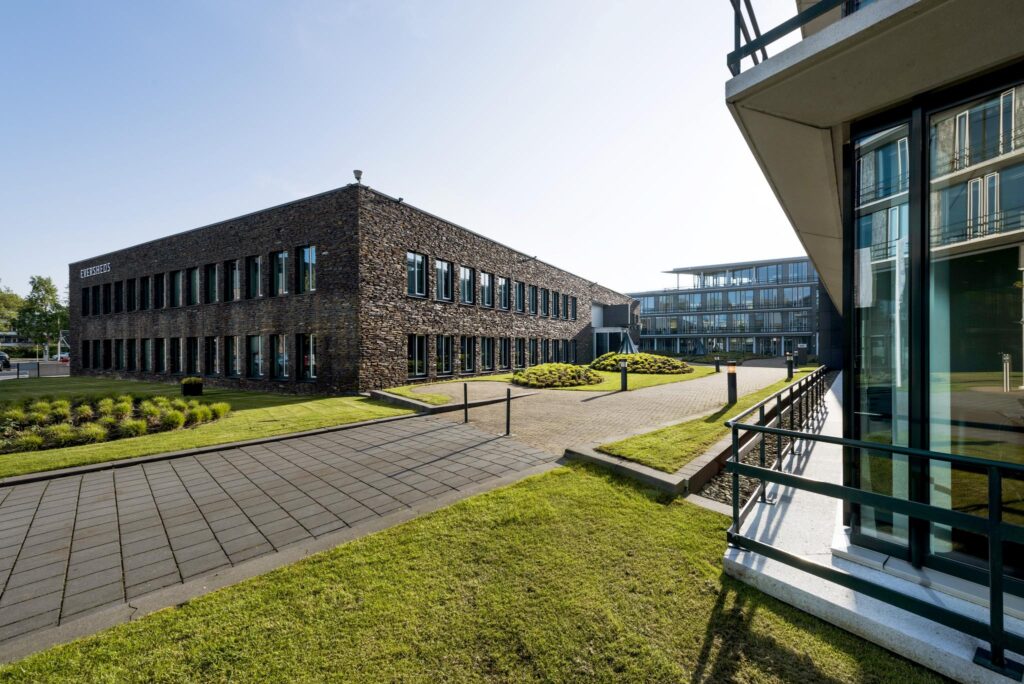 Modern kantoorgebouw aan de De Cuserstraat in Amsterdam met een gevel van natuursteen en een verzorgde tuin.
