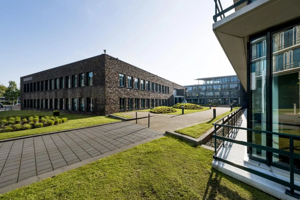 Modern kantoorgebouw aan de De Cuserstraat in Amsterdam met een gevel van natuursteen en een verzorgde tuin.