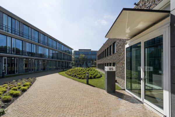 Modern kantoorgebouw aan de De Cuserstraat 85 met een verzorgde binnentuin en glazen gevels.