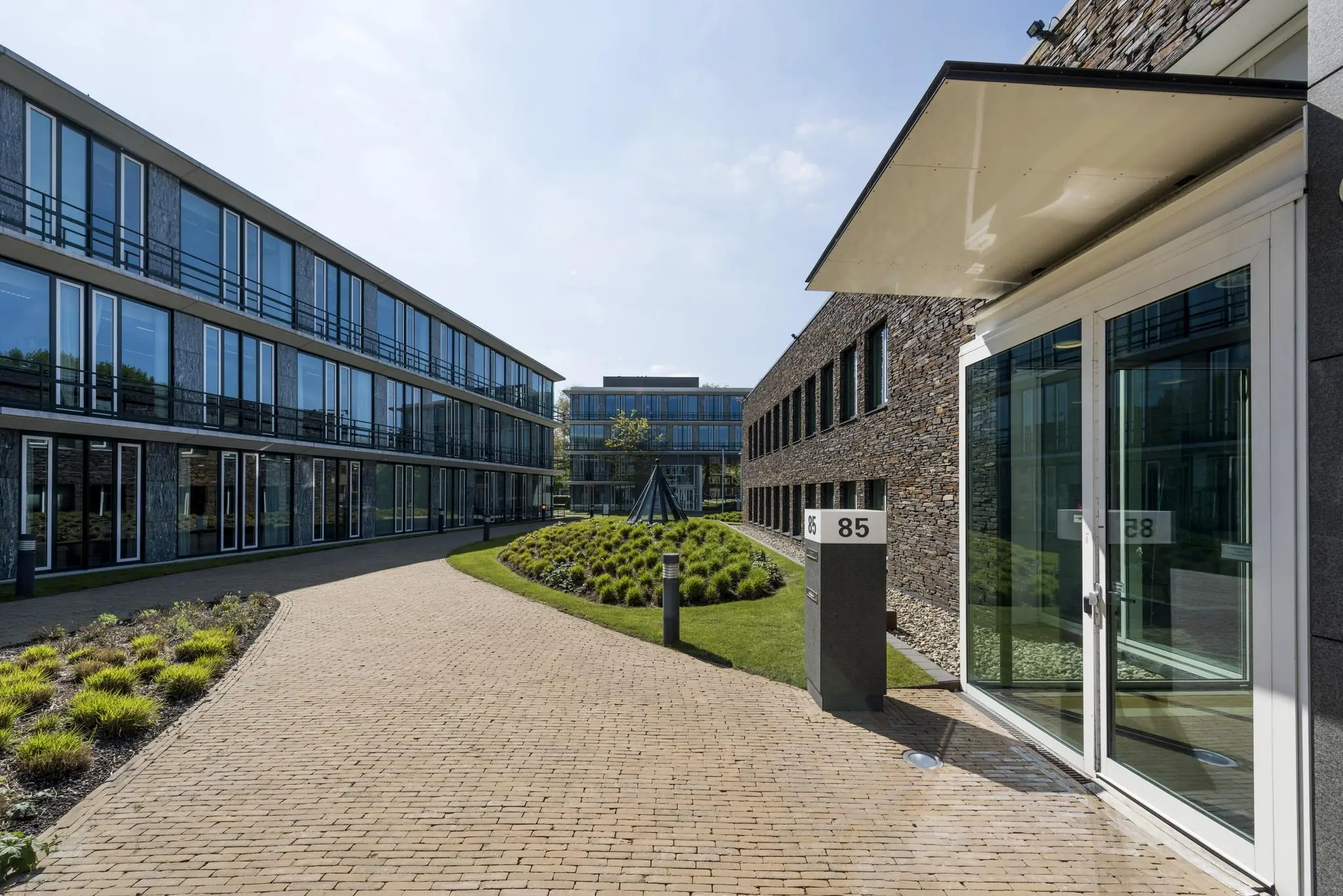 Modern kantoorgebouw aan de De Cuserstraat 85 met een verzorgde binnentuin en glazen gevels.