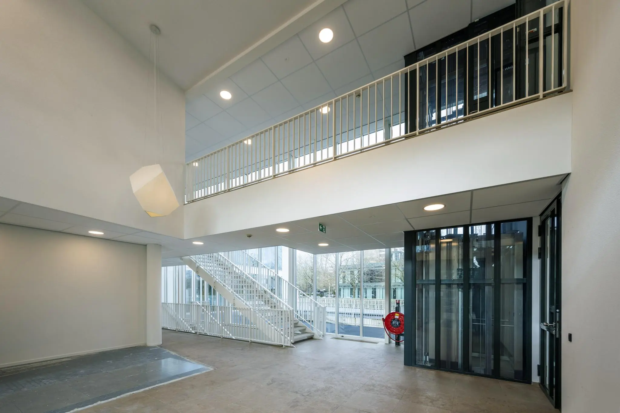 Moderne, lichte entreehal van een gebouw aan de De Cuserstraat met een trap, lift en grote ramen.