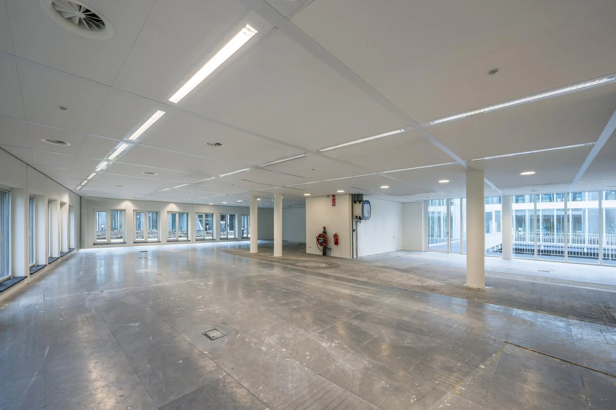 Leeg kantoorpand aan de De Cuserstraat met grote ramen en betonnen vloer.