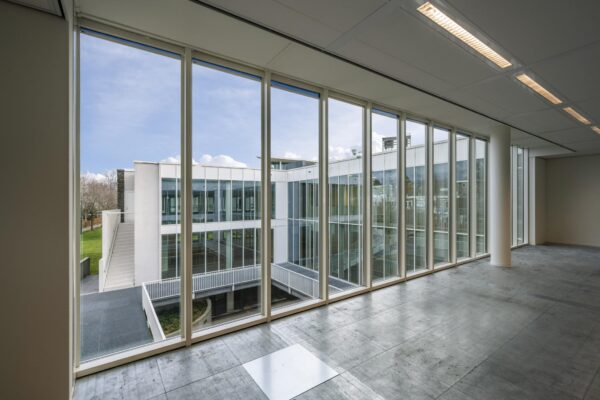 Uitzicht vanuit een lege kantoorruimte op de moderne glazen gevel van een gebouw aan de De Cuserstraat.