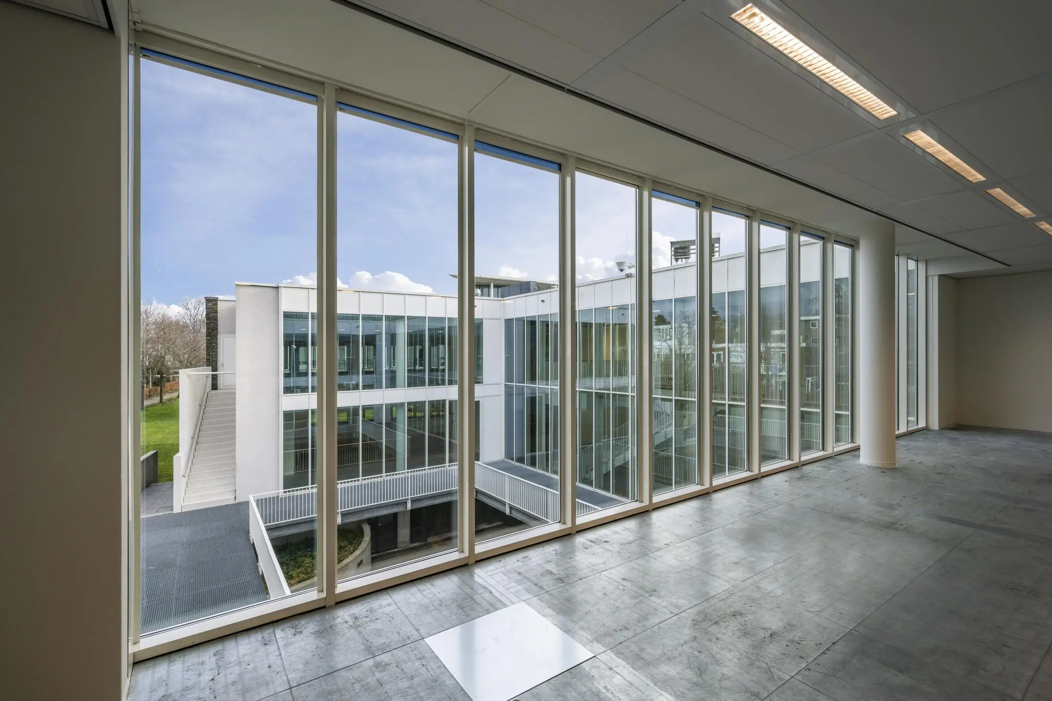 Uitzicht vanuit een lege kantoorruimte op de moderne glazen gevel van een gebouw aan de De Cuserstraat.