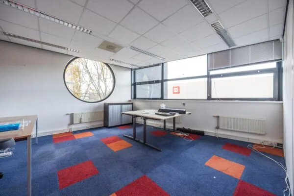 Kantoorruimte aan de Atoomweg met kleurrijk tapijt, ronde en rechthoekige ramen en uitzicht op een Picnic-gebouw.