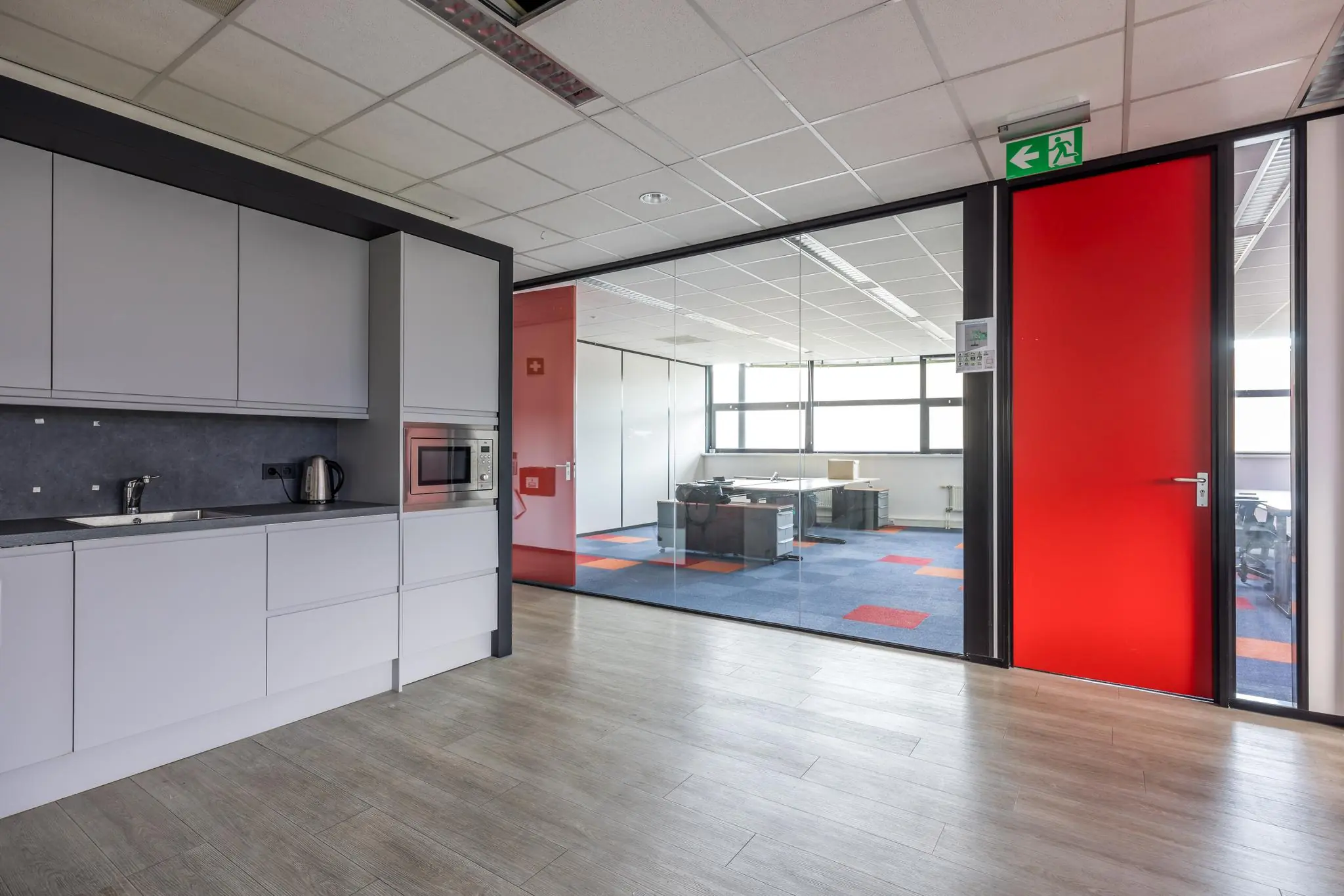 Moderne kantoorruimte aan de Atoomweg met een pantry, glazen vergaderruimte en opvallende rode deur.