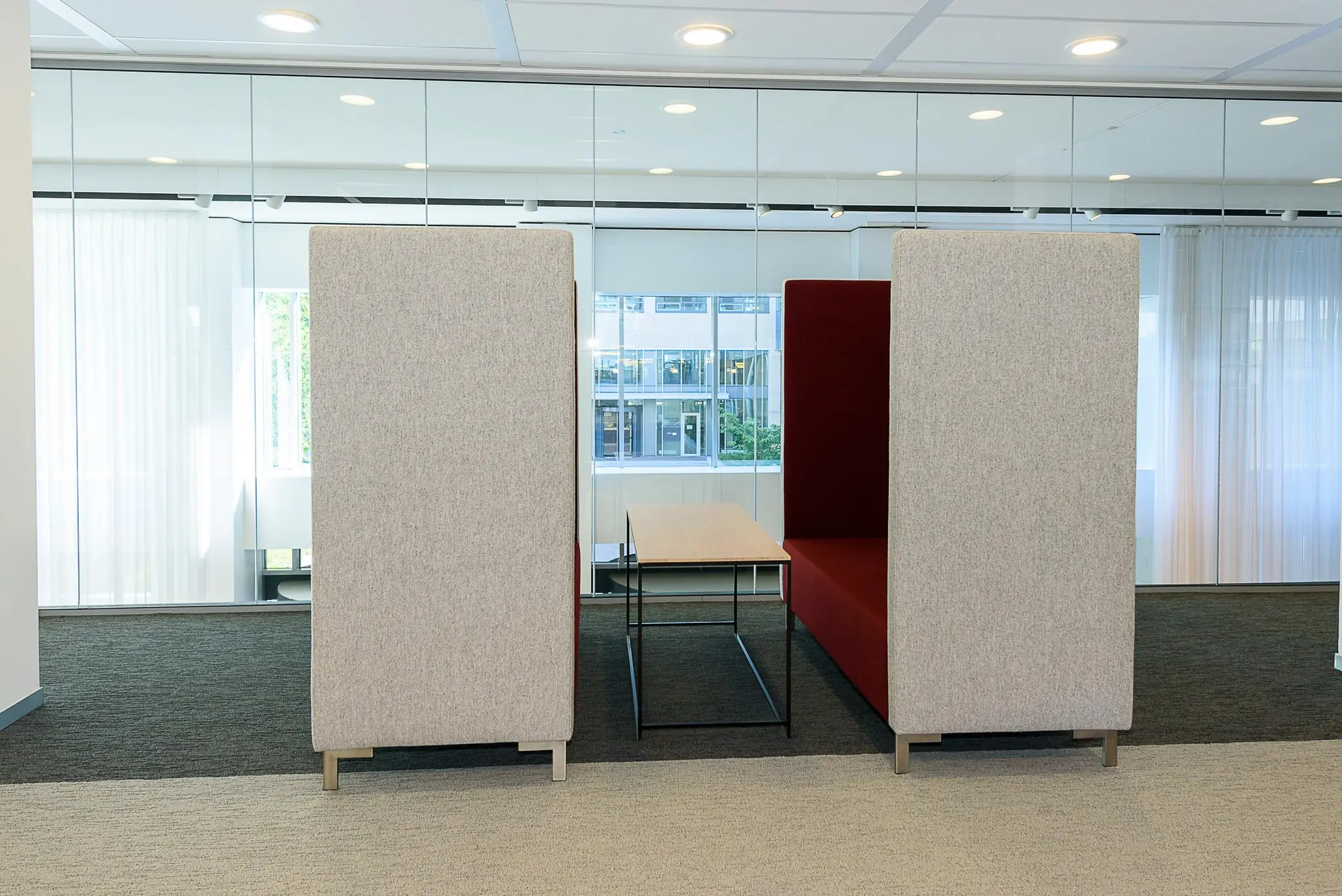 Moderne zithoek met hoge akoestische banken en een houten tafel op het Daalseplein kantoor.