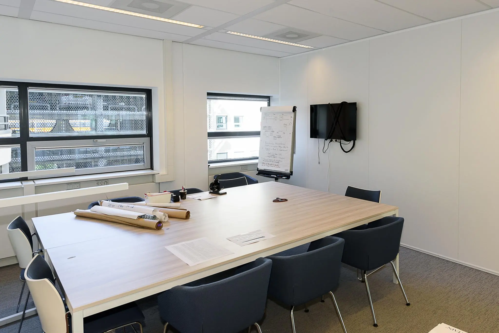 Vergaderruimte aan het Daalseplein met een tafel, stoelen, whiteboard, tv-scherm en bouwtekeningen.