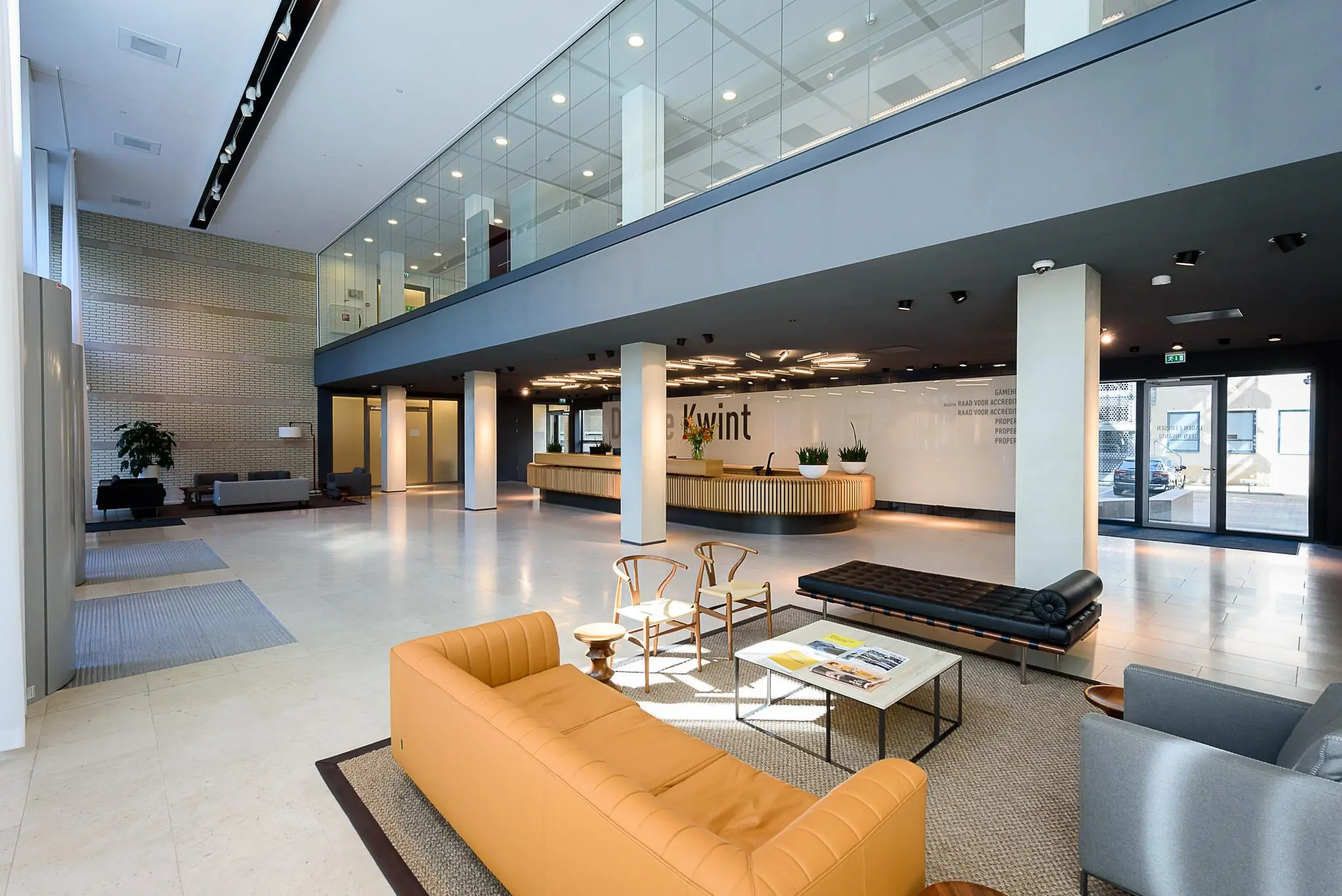 Moderne ontvangsthal van het kantoorgebouw aan het Daalseplein met zithoeken, balie en glazen bovenverdieping.