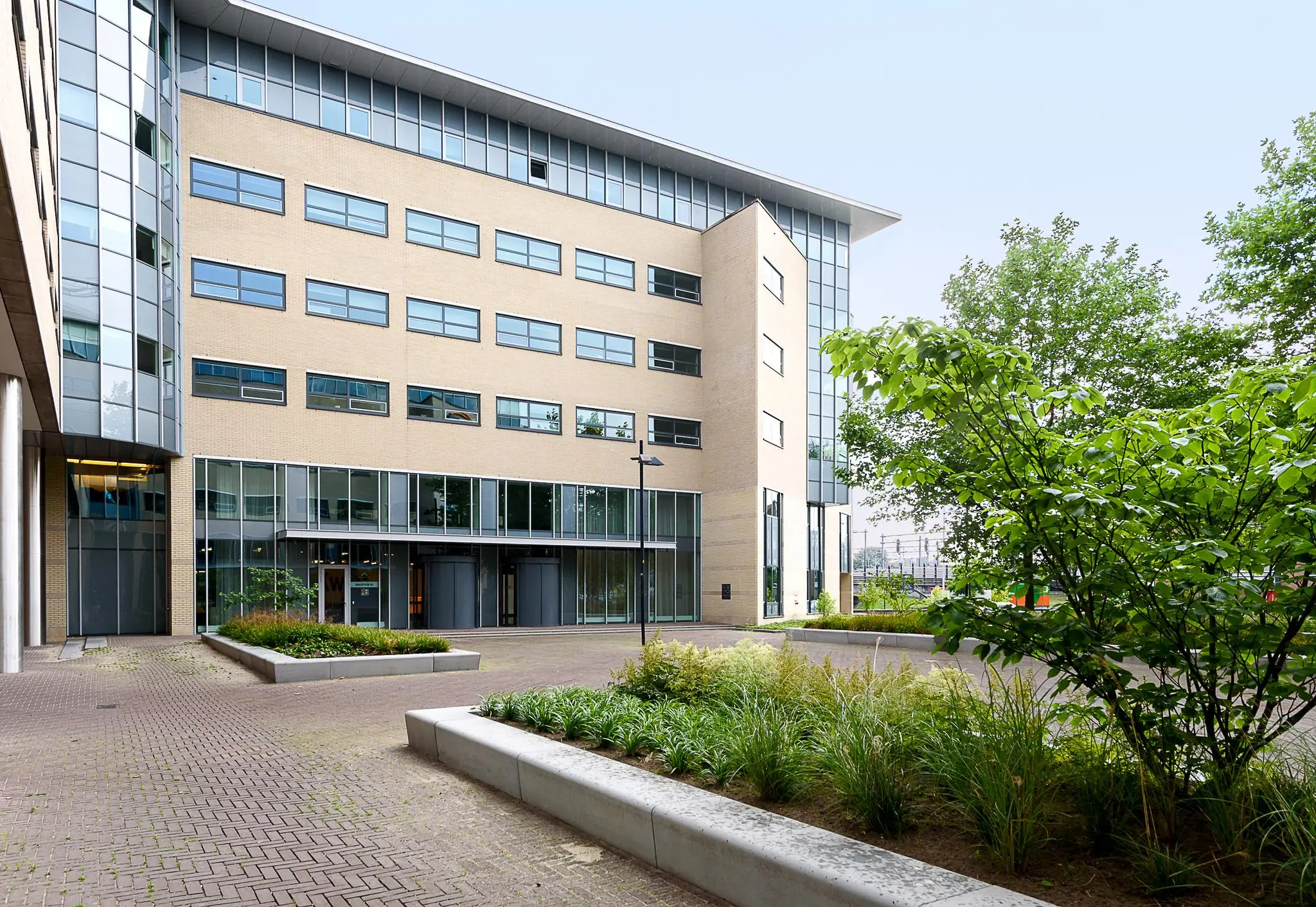 Modern kantoorgebouw aan het Daalseplein met een betegeld plein en groene beplanting op de voorgrond.