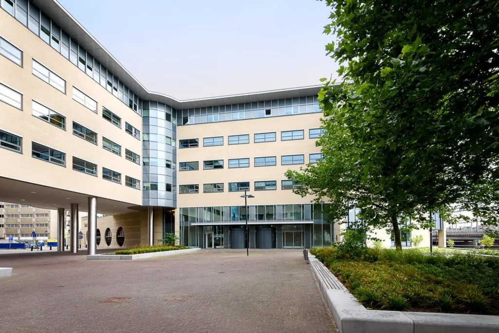 Ingang van een modern kantoorgebouw aan het Daalseplein met veel glas en een groen aangelegd plein.