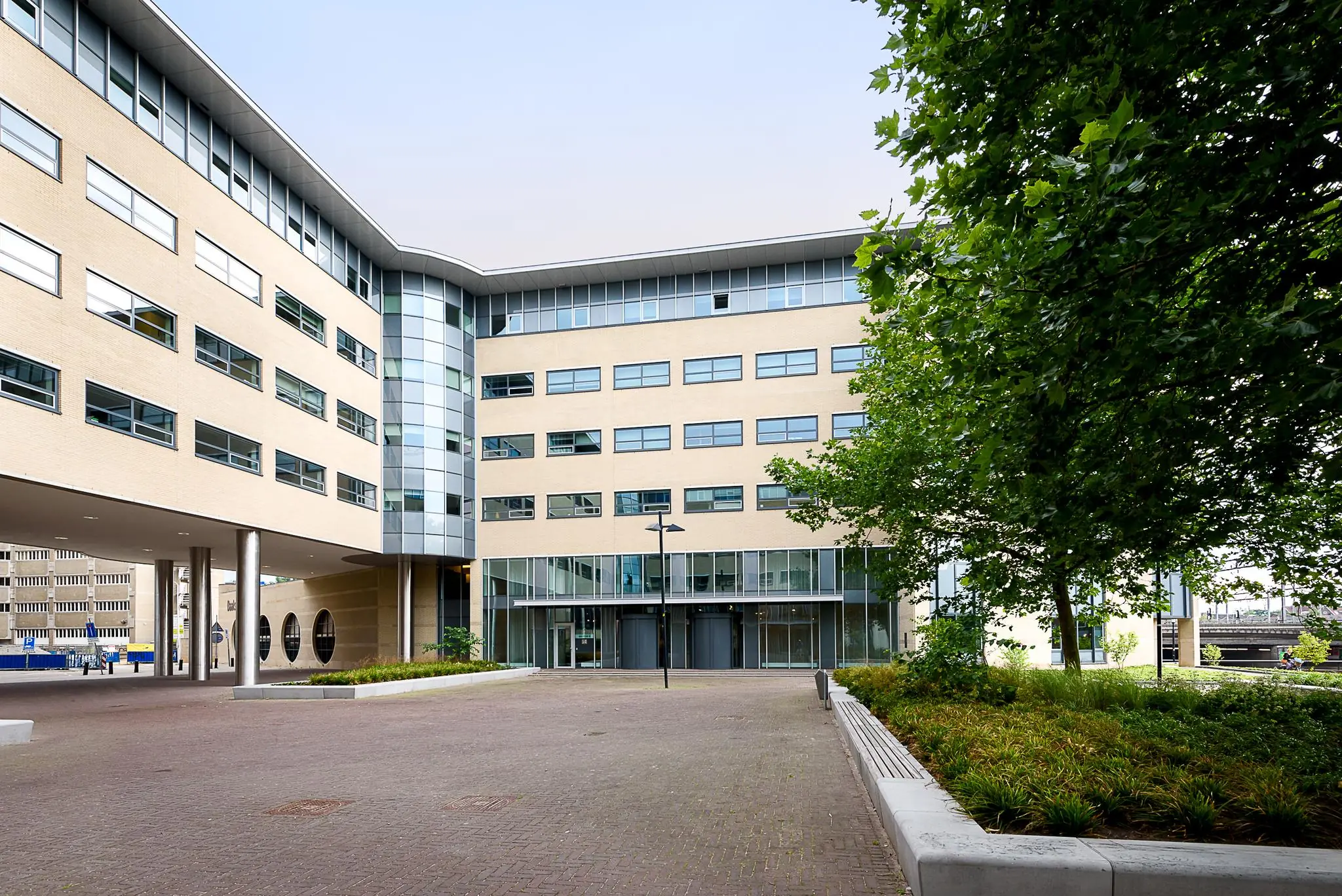 Ingang van een modern kantoorgebouw aan het Daalseplein met veel glas en een groen aangelegd plein.