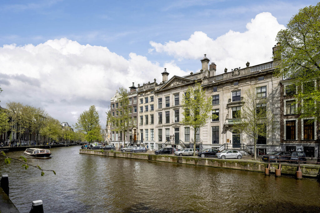 Monumentale grachtenpanden aan de Herengracht in Amsterdam met een rondvaartboot op het water.