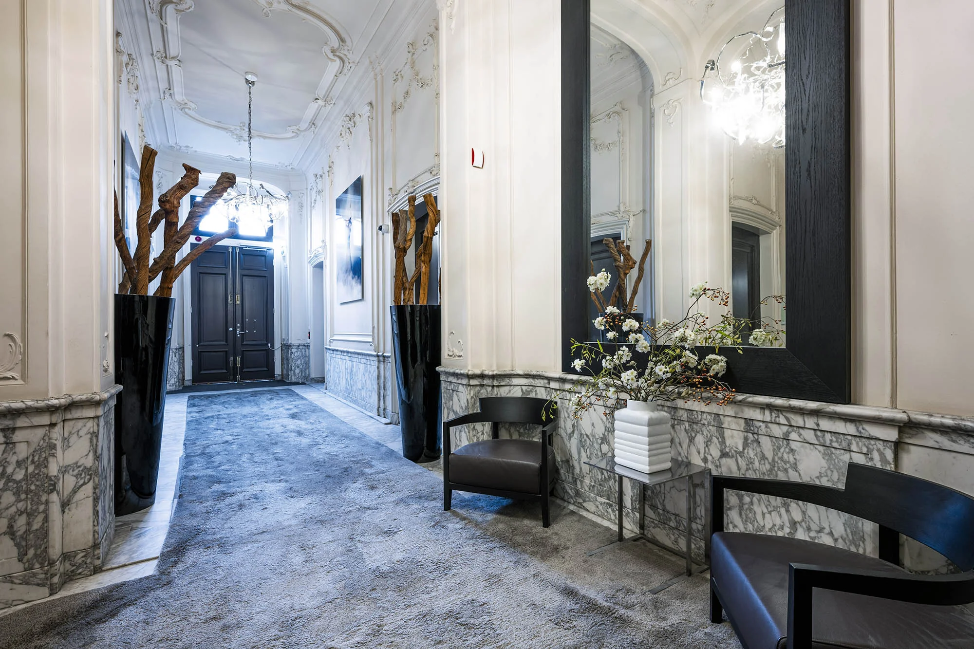 Luxe entreehal aan de Herengracht met marmeren muren, decoratieve plafondlijsten en moderne meubelen.