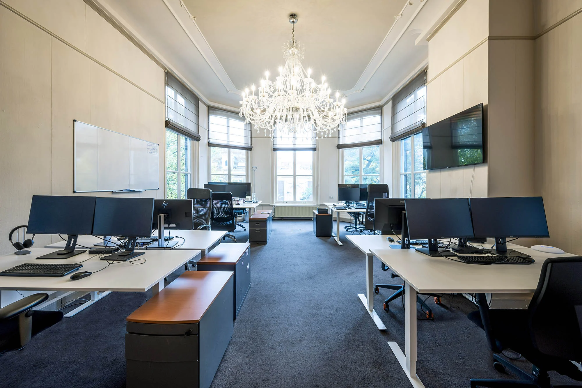Modern kantoor aan de Herengracht met multiple bureaus, computers en een grote kristallen kroonluchter.