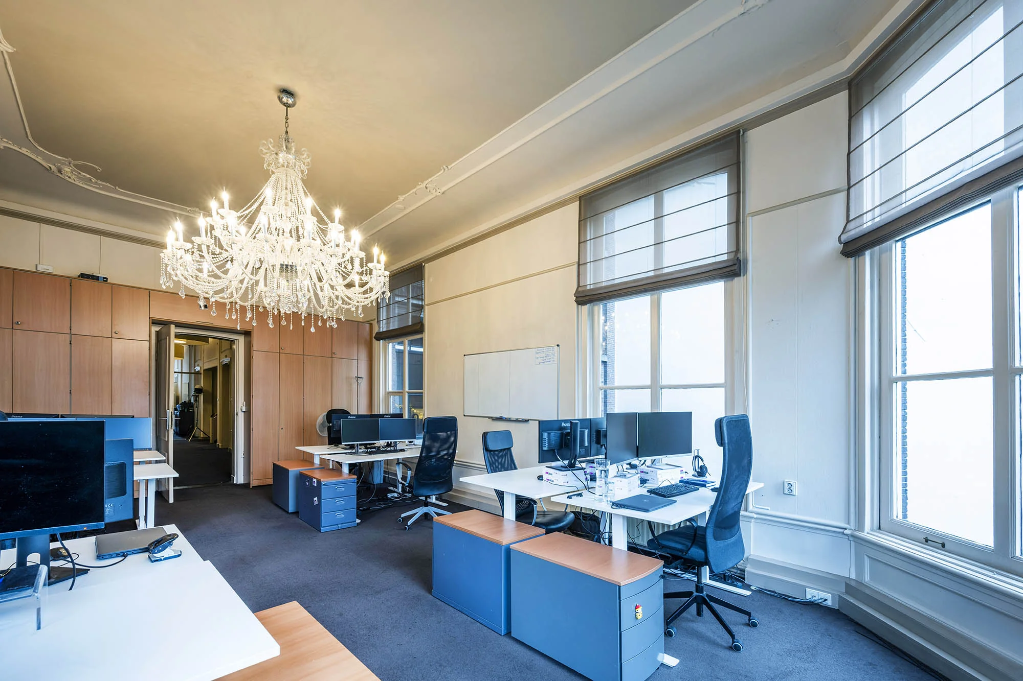 Modern kantoorinterieur aan de Herengracht met werkplekken, hoge ramen en een grote kristallen kroonluchter.