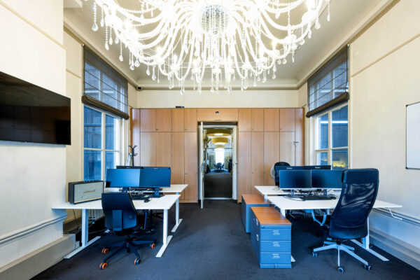 Moderne kantoorruimte aan de Herengracht met bureaus, computers en een grote kristallen kroonluchter aan het plafond.