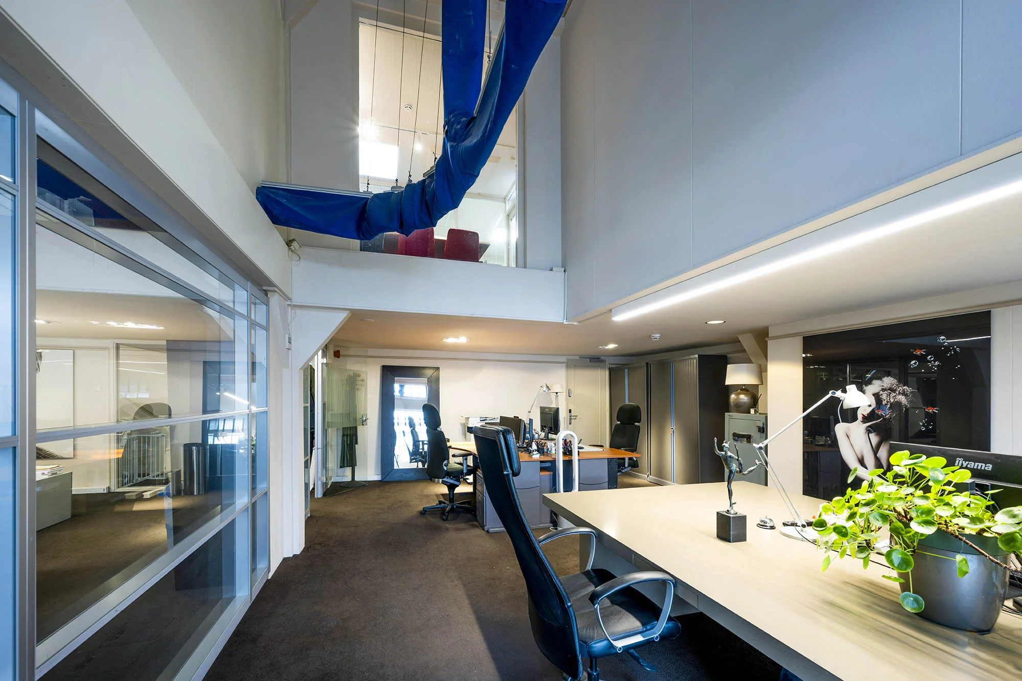 Modern kantoorinterieur aan de Herengracht met open werkplekken, glazen wanden en een opvallend kunstobject aan het plafond.