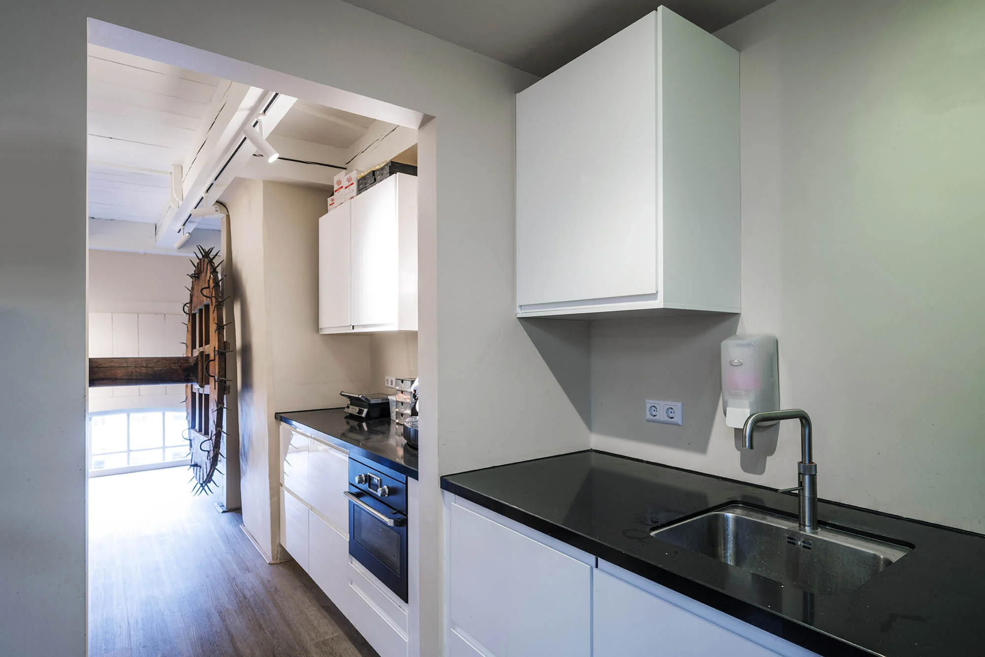 Moderne kitchenette in Herengracht met witte kasten, zwart werkblad en roestvrijstalen kraan.