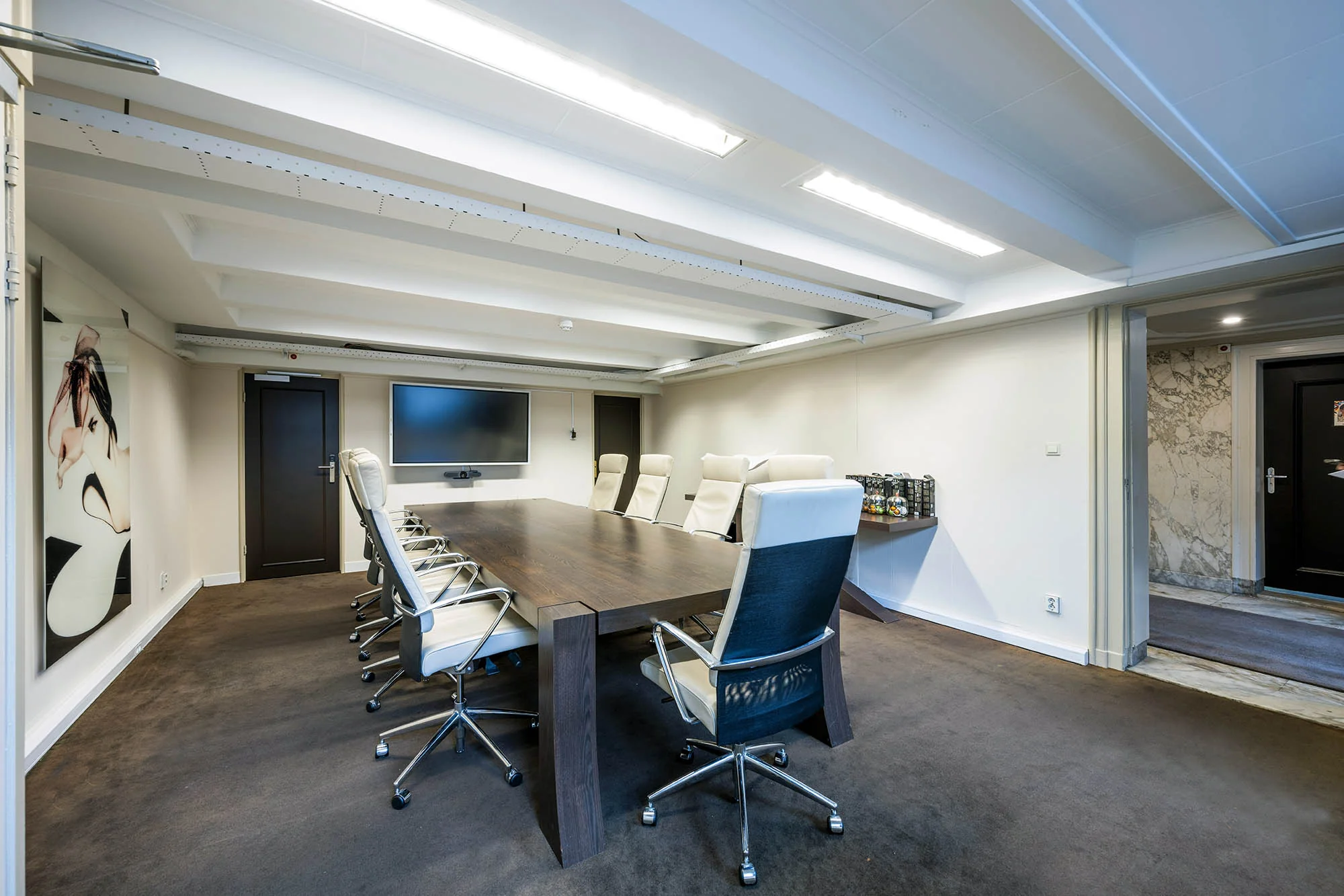 Vergaderruimte aan de Herengracht met modern interieur, grote houten tafel, witte bureaustoelen en een flatscreen aan de muur.