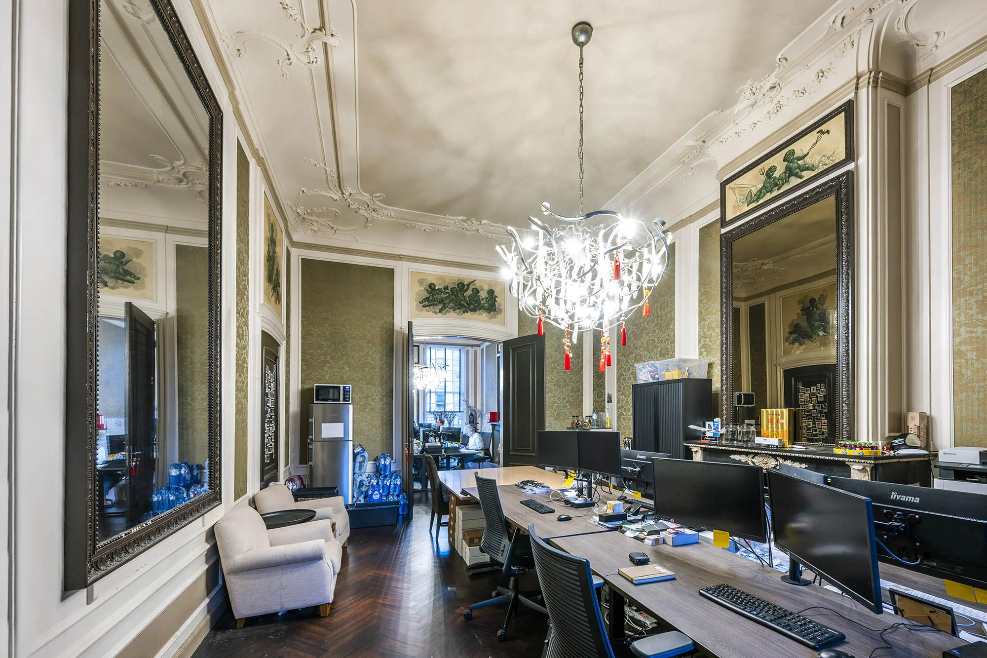 Klassiek ingerichte kantoorruimte aan de Herengracht met hoge plafonds, sierlijke kroonluchter en meerdere werkplekken met computers.