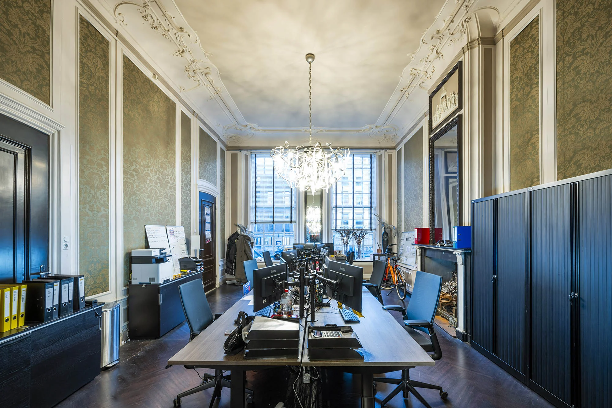 Modern ingericht kantoor met meerdere werkplekken in een klassiek pand aan de Herengracht, met hoge plafonds en een opvallende kroonluchter.