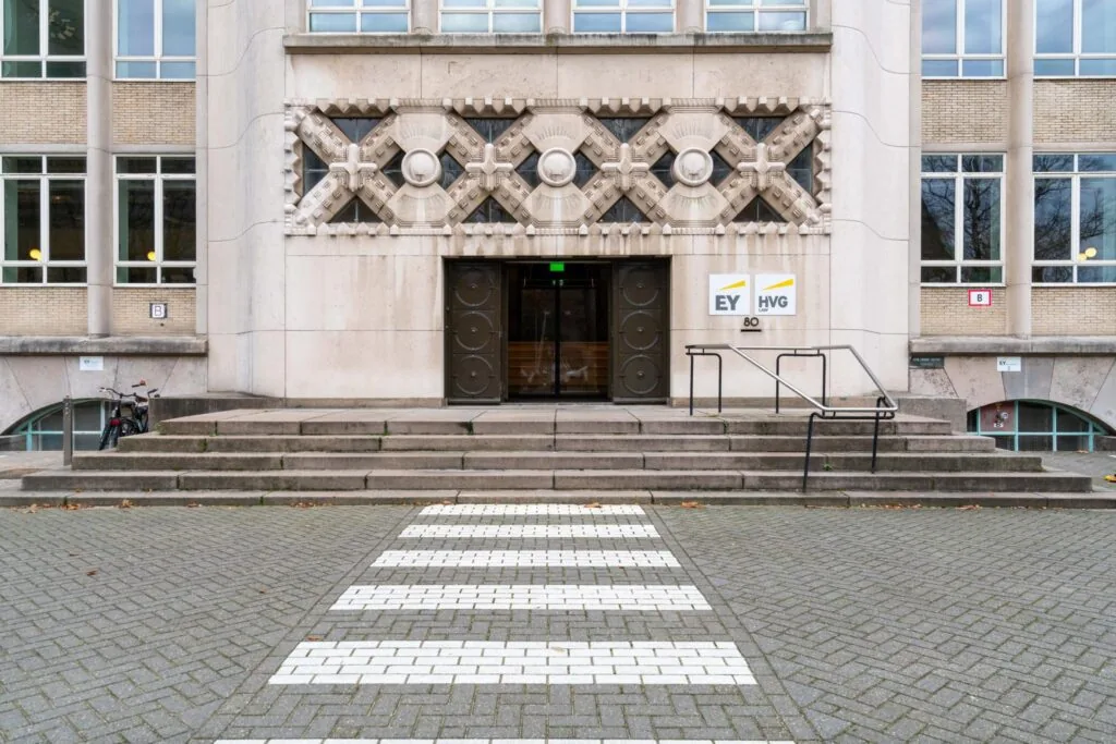 Ingang van het kantoorgebouw aan de Wassenaarseweg 80 met EY en HVG Law borden naast de deur.