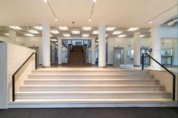 Ingang van een modern kantoorgebouw aan de Wassenaarseweg met brede trap, pilaren en een centrale houten trap naar de eerste verdieping.