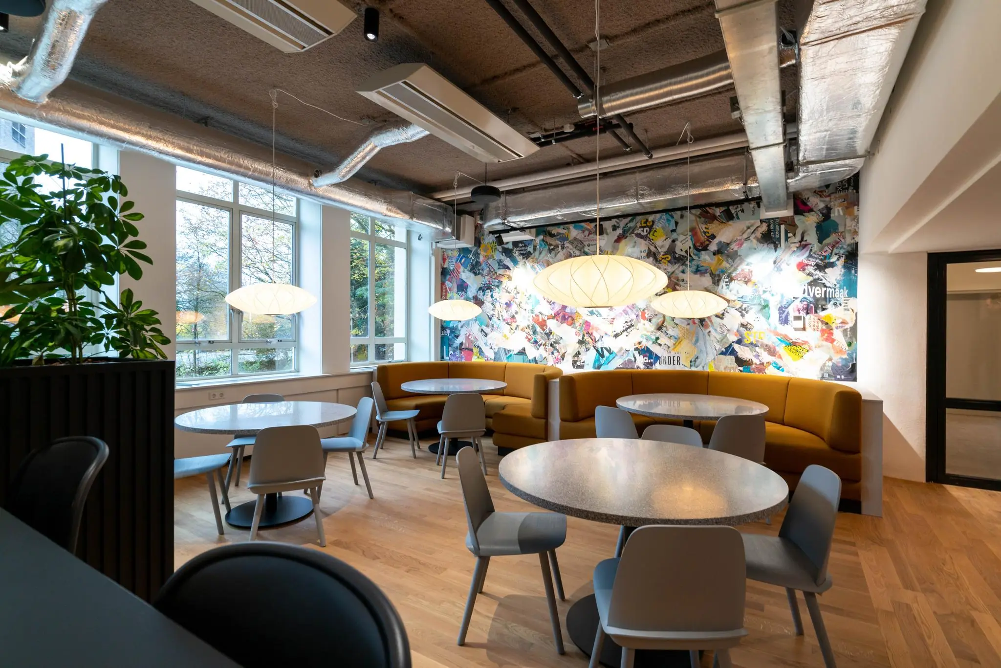 Moderne en kleurrijke kantineruimte aan de Wassenaarseweg met ronde tafels, designverlichting en een opvallende kunstmuur.