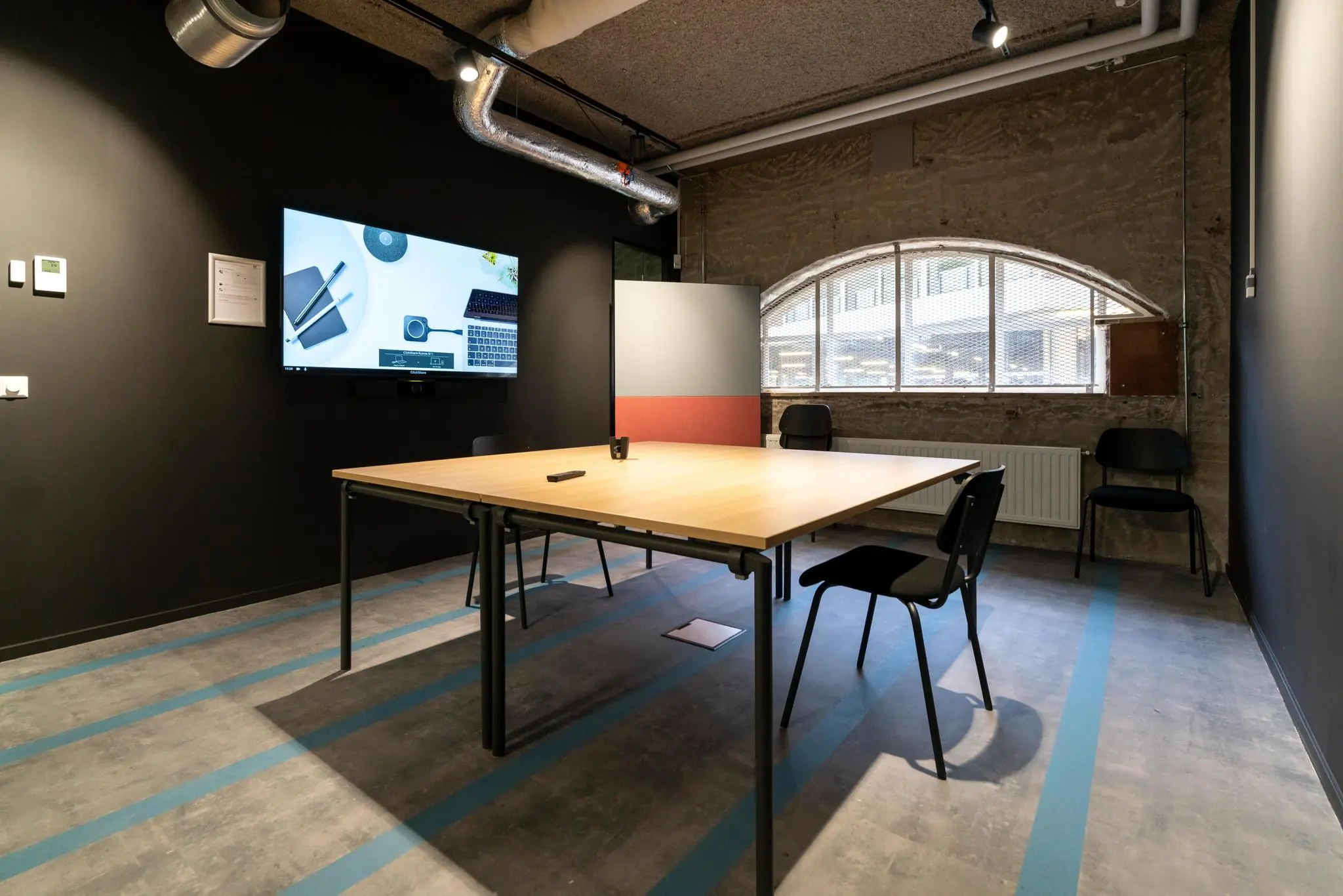 Moderne vergaderruimte aan de Wassenaarseweg met een houten tafel, stoelen, een flatscreen en industrieel interieur.